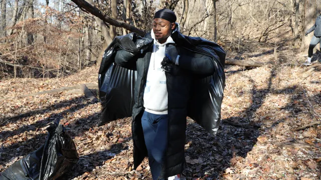 A person carrying two trash bags and walking in the woods.