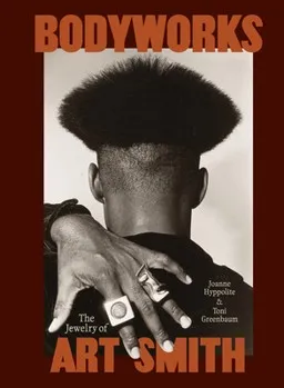 Book cover titled BODYWORKS. A black-and-white photograph shows the back of a person’s head with a sculptural high-top hairstyle and a hand draped across the shoulder, adorned with several large rings. The design is framed by a deep reddish-brown border, with the subtitle, The Jewelry of Art Smith, and contributors’ names displayed on the cover.