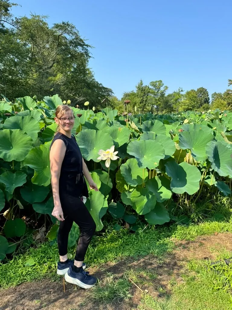 Alina stands smiling beside the lotus ponds on a summer outing.