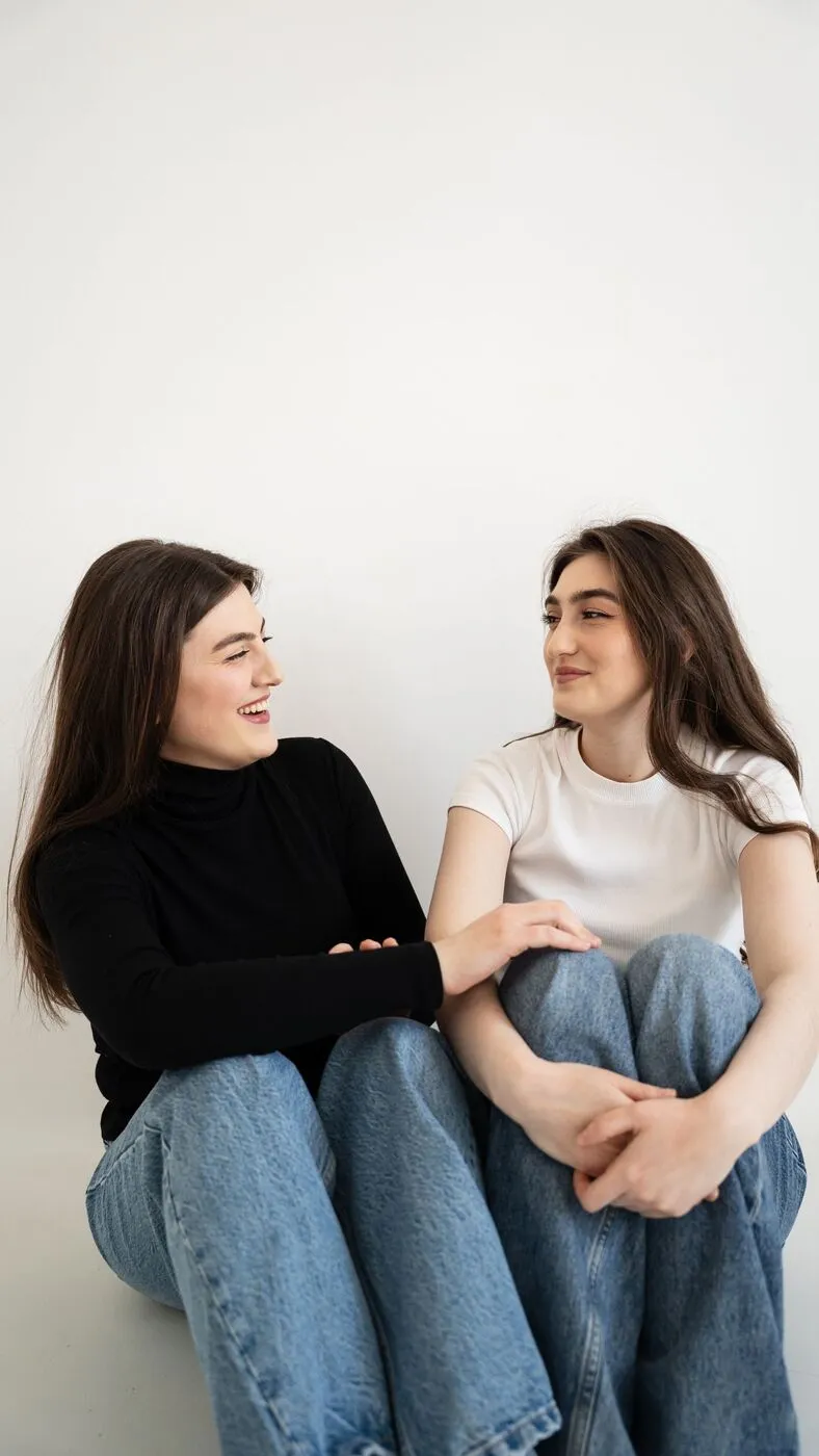 Dos jóvenes sentadas juntas en el suelo, una de ellas riendo.