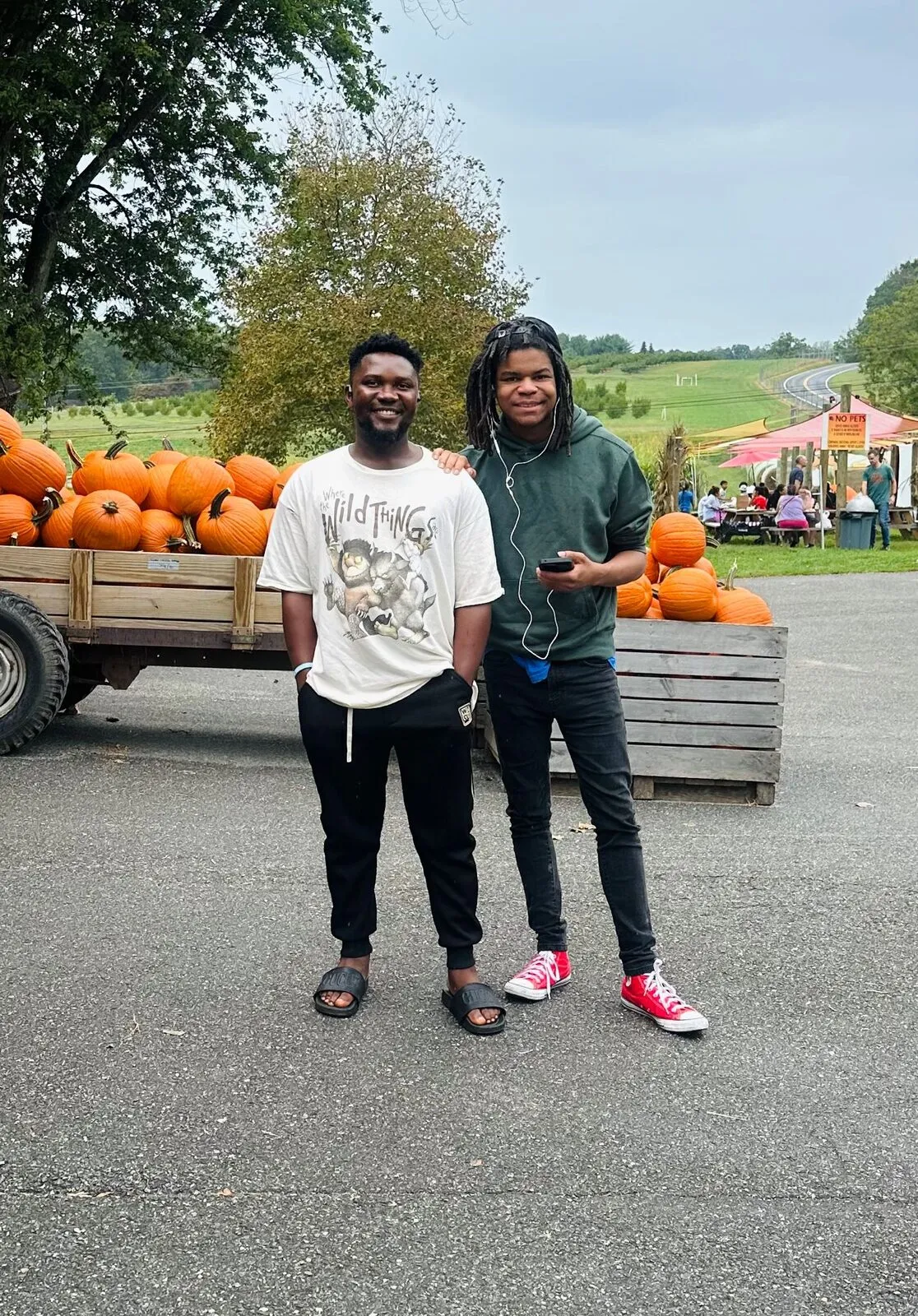 Mr. Brinet and David Jackson stand together in front of a trailer of pumpkins at a fall farm outing.