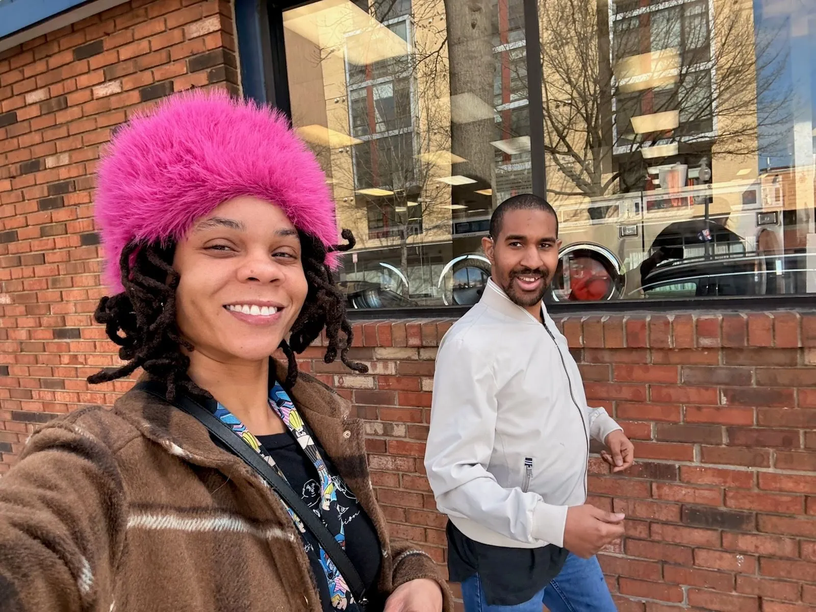 Kha'Deisha Warren takes a smiling selfie with a colleague outside a brick building.