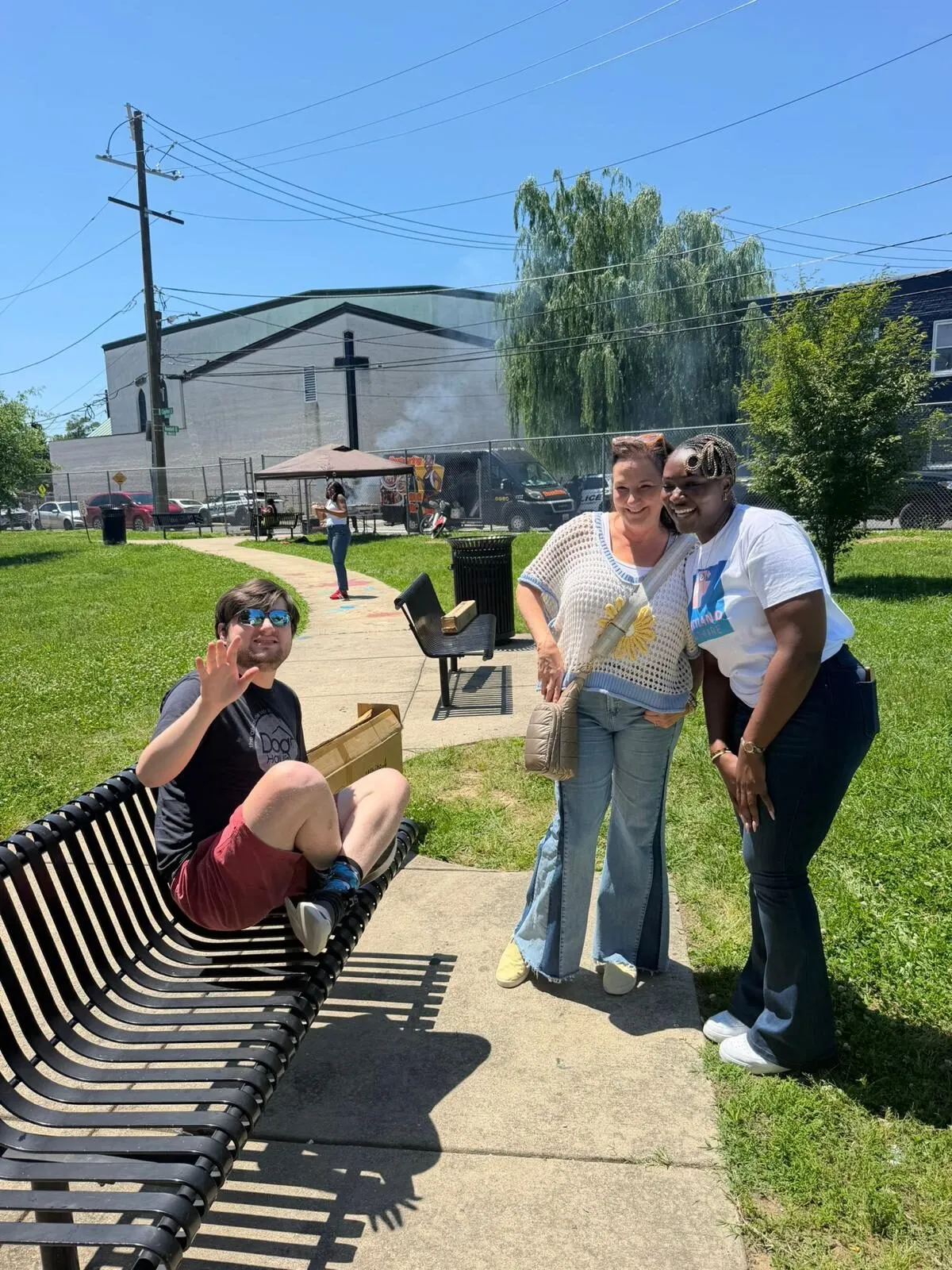 Two Mercyland staff members share a laugh with a man they support during a sunny afternoon outing in a DC park.