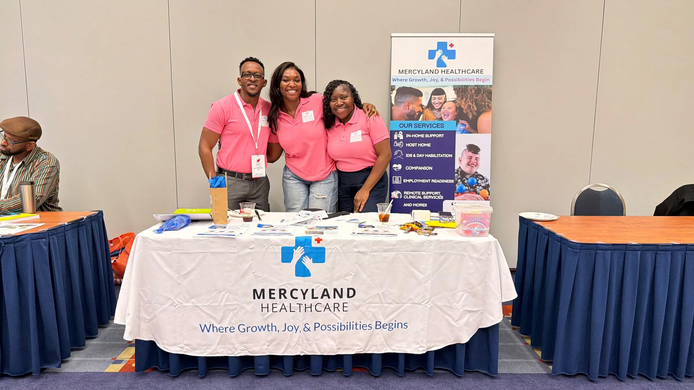 Three members of the Mercyland team in pink shirts at the Mercyland information table at a community event.