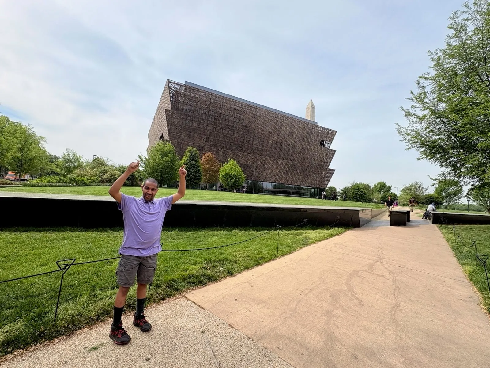 A man raises both arms in celebration on the path outside the National Museum of African American History and Culture in Washington, DC.