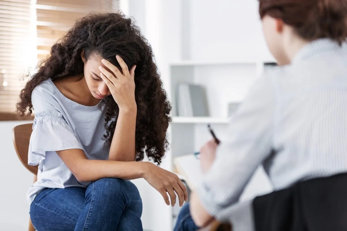 A young woman holds her head in her hands while a counselor listens and takes notes.