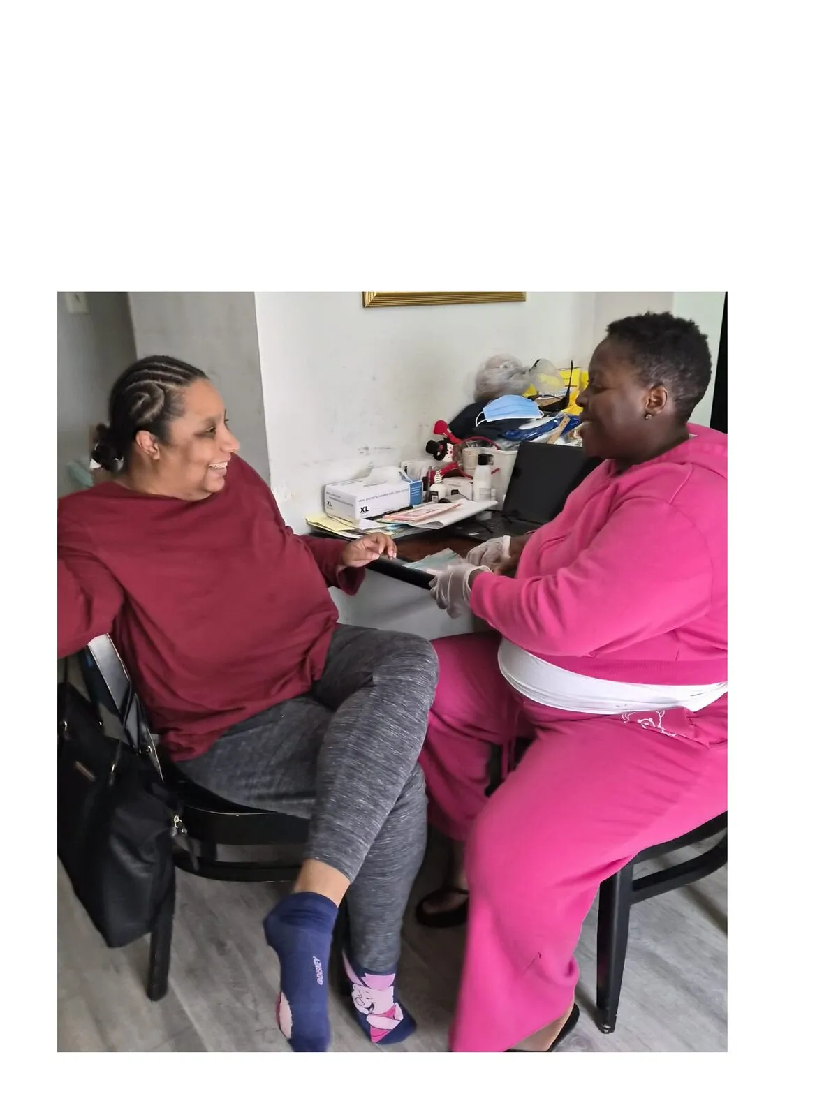 A Mercyland Direct Support Professional in pink scrubs sits with the woman she supports during a home visit.