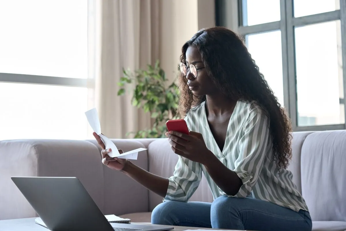 Una mujer revisa documentos y su teléfono en casa.