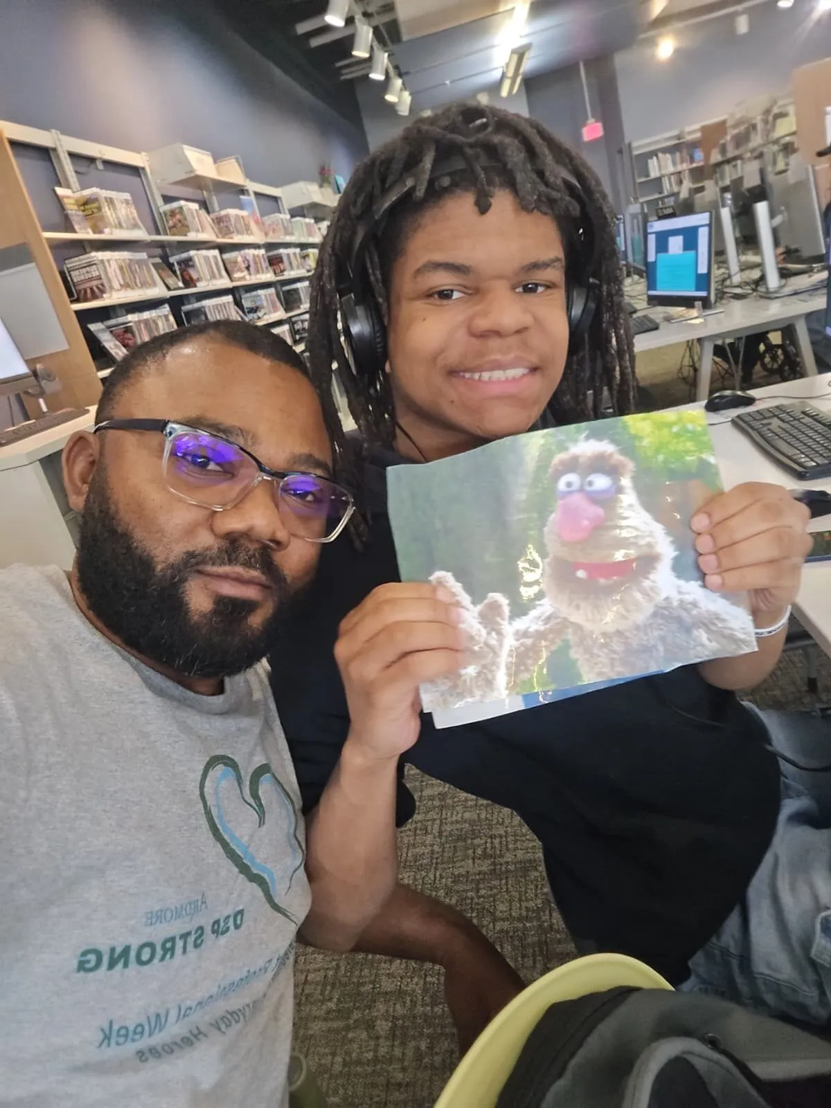 Mr. Yannick and David Jackson take a selfie at the library, David holding up a picture he found.