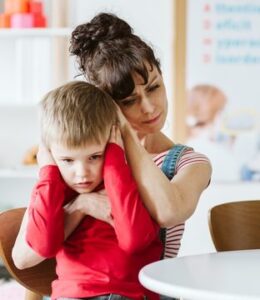 A woman holds a young boy close as he covers his ears with his hands.