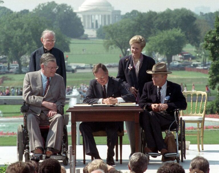 President George H. W. Bush signing the Americans with Disabilities Act into law on the White House South Lawn, July 26, 1990, seated beside disability rights advocates.