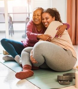 Dos mujeres sentadas juntas en el suelo se abrazan y ríen.